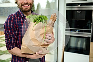 Close-up eco paper bag, craft cardboard packet with greens, salads, healthy food, whole grain baguette bread in hands of handsome