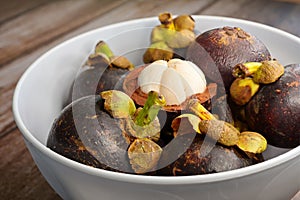 Close-up of edible flesh of an open mangosteen fruit & a bowl of ripe whole fruits in a white bowl