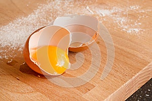 Close up egg, yolk in eggshell, flour on a wooden background