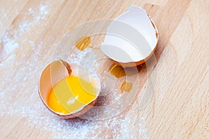 Close up egg, yolk in eggshell, flour on a wooden background