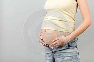 Close up of elastic maternity band dressed on pregnant woman to reduce backache at gray background with copy space. Orthopedic