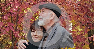 Close-up elderly couple, bearded husband with gray haire hugging sad wife with bouquet of autumn leaves, consoling