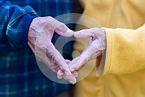 Close-up of the elderly couple`s hand showing a heart-shaped symbol with fingers. Concept of aged people and love