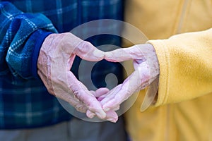 Close-up of the elderly couple showing making a heart with fingers. Concept of aged people and love