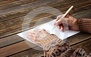 Close up of elderly male hands on wooden table . writing on blank paper