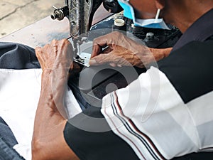 Close-up of an elderly man's fixing a pant into a sewing machine.