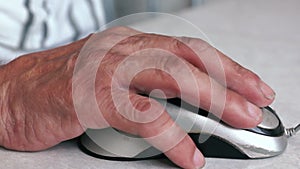 Close-up of an elderly man`s hand clicking a computer mouse while working on a gadget. Adult seniors and digital devices. Selectiv