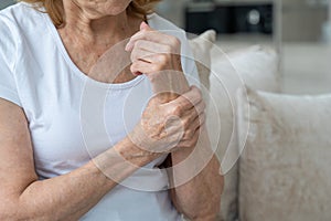 Close-up elderly woman suffering from arthritis of the hands sitting on the couch. The concept of mental health and care