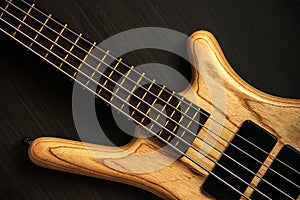 Close up of electric bass guitar with five strings. Detailed view of wooden varnished texture of musical instrument