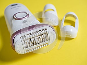 Close-up of the electric epilator for hair removal of white color on a yellow background. Next to the additional nozzle. Beauty