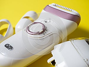 Close-up of the electric epilator for hair removal of white color on a yellow background. Next to the additional nozzle. Beauty