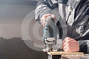 Close-up electric jigsaw in the hands of a worker in a home workshop. Starting a business. Craftsman