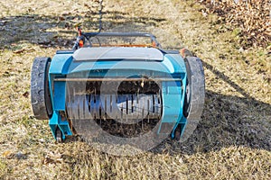 Close-up of an electric lawn aerator with a barbed wire nozzle on yellow grass in a garden on a spring day.