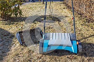 Close-up of an electric lawn aerator and a removed basket of collected dry yellow grass.