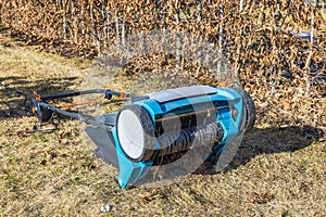 Close-up of an electric lawn aerator with a wire attachment gathering dry grass in garden on spring day.