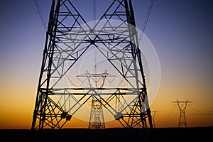 Close up of electrical transmission tower with another tower in distance against desert sunset sky