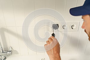 Close up of electrician using screwdriver while installing new electrical socket on home kitchen