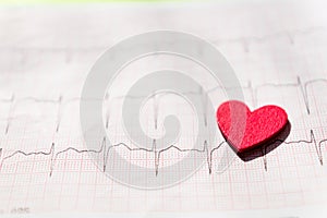 Close up of an electrocardiogram in paper form vith red wooden heart. ECG or EKG paper  background texture.  medical and