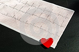 Close up of an electrocardiogram in paper form vith red wooden heart. ECG or EKG paper on black  background.  medical and