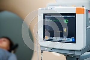 Close up electrocardiograph showing patient heart rate with pacient lying in computed tomography room. Selective focus