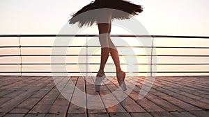 Close up of an elegant ballet dancer`s legs, stepping on a wooden embankment on tip toes in pointes. Black ballet tutu