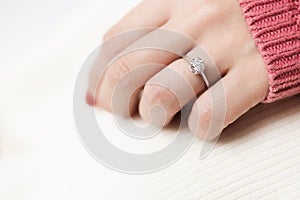 Close up of an elegant engagement diamond ring on woman finger with pink sweater winter clothe
