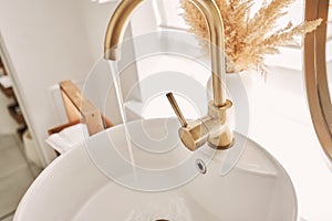 Close-up of an elegant golden faucet in the bathroom sink next to stylish decorations. A beautiful sink with a golden