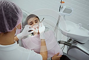 Close-up of elementary aged boy with opened mouth and cheek retractor at dental appointment in contemporary modern dental clinic.