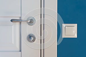 Close-up elements of the interior of the apartment. Detail of a white interior door with a chrome door handle and latch, light swi