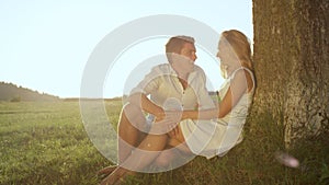 CLOSE UP: Embraced young couple in love sitting under a beautiful tree in meadow