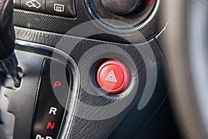 Close-up of an emergency button with a white triangle icon on the red plastic of a car dashboard. Signal of breakage, problem, or