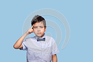 Close up  emotional portrait of a serious boy thinking of anything.  He holds his index finger at the temple showing this gesture