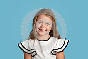 Close up emotional portrait of young blonde smiling girl wearing white blous with black strips on blue background in studio