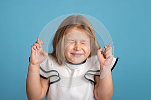 Close up emotional portrait of young blonde smiling girl wearing white blous with black strips on blue background in studio. She