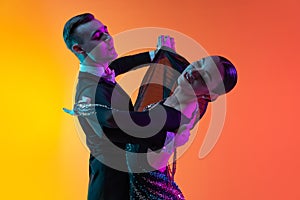 Close-up emotive dancing couple, beautiful man and woman dancing waltz isolated over gradient orange pink background in