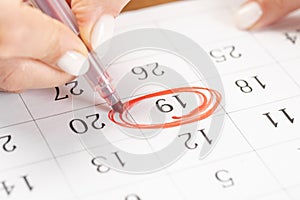 Close up on employee woman hand using red pen to writing schedule on 19th day of the monthcalendar 2022 to make an appointment