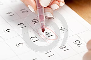 Close up on employee woman hand using red pen to writing schedule on 19th day of the monthcalendar 2022 to make an appointment