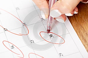 Close up on employee woman hand using red pen to writing schedule on 30 day calendar 2022 to make an appointment meeting or manage