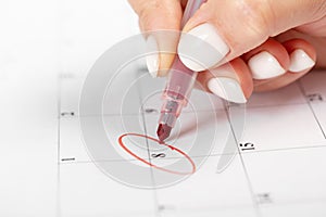 Close up on employee woman hand using red pen to writing schedule on calendar 2022 to make an appointment meeting or manage