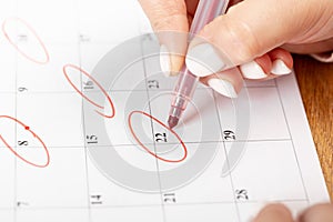 Close up on employee woman hand using red pen to writing schedule on calendar 2022 to make an appointment meeting or manage