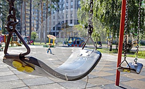 Close up empty baby swing in the park. New chain swing. Set of black swing chains on a modern playground. Focus on the swing in