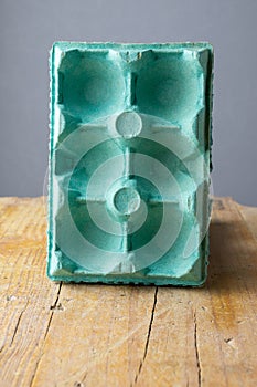 Close-up of empty blue egg carton on rustic wooden board and gray background, vertical