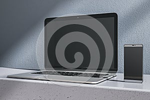 Close up of empty laptop and mobile phone on gray desk. Concrete wall background. Device presentation and online education concept