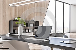 Close up of empty laptop screen on desktop in modern wooden and concrete designer office interior with furniture, window with