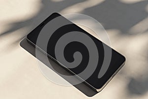 Close up of empty mobile phone on light surface with leaf shadows. Presentation concept. Mock up