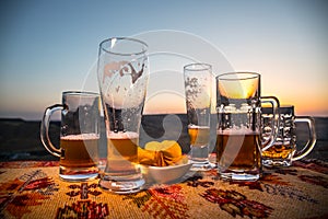 Close up empty mugs of beer on a sunrise background with mountains. Beer party is over concept.