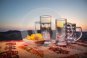 Close up empty mugs of beer on a sunrise background with mountains. Beer party is over concept.