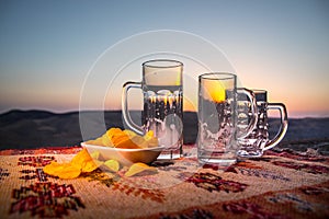 Close up empty mugs of beer on a sunrise background with mountains. Beer party is over concept.