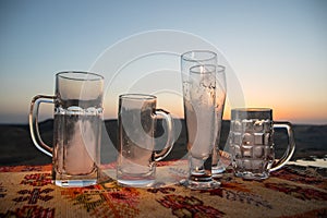 Close up empty mugs of beer on a sunrise background with mountains. Beer party is over concept.