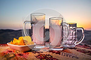 Close up empty mugs of beer on a sunrise background with mountains. Beer party is over concept.